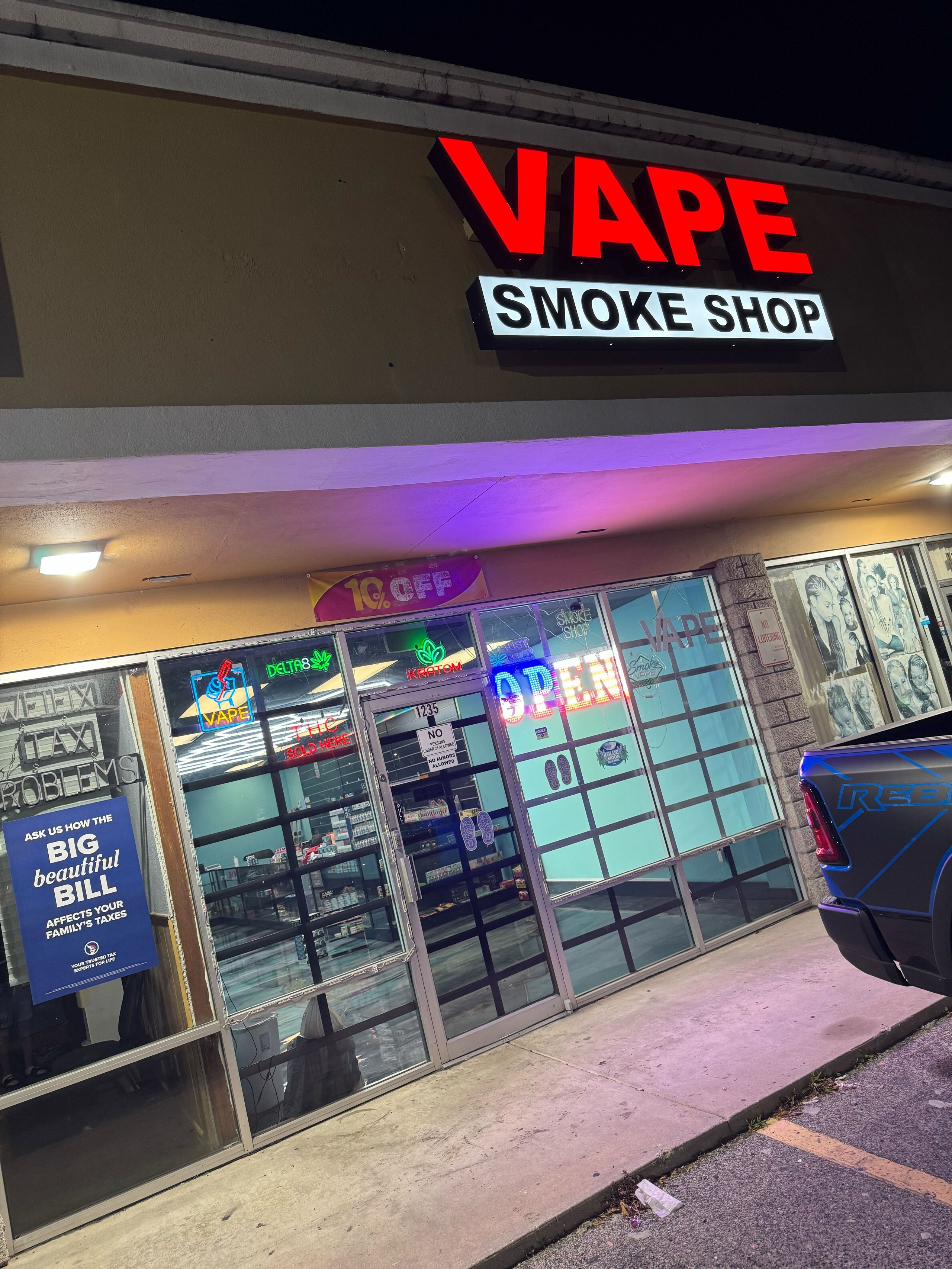 Vape smoke shop storefront at night with illuminated red sign and glass doors.