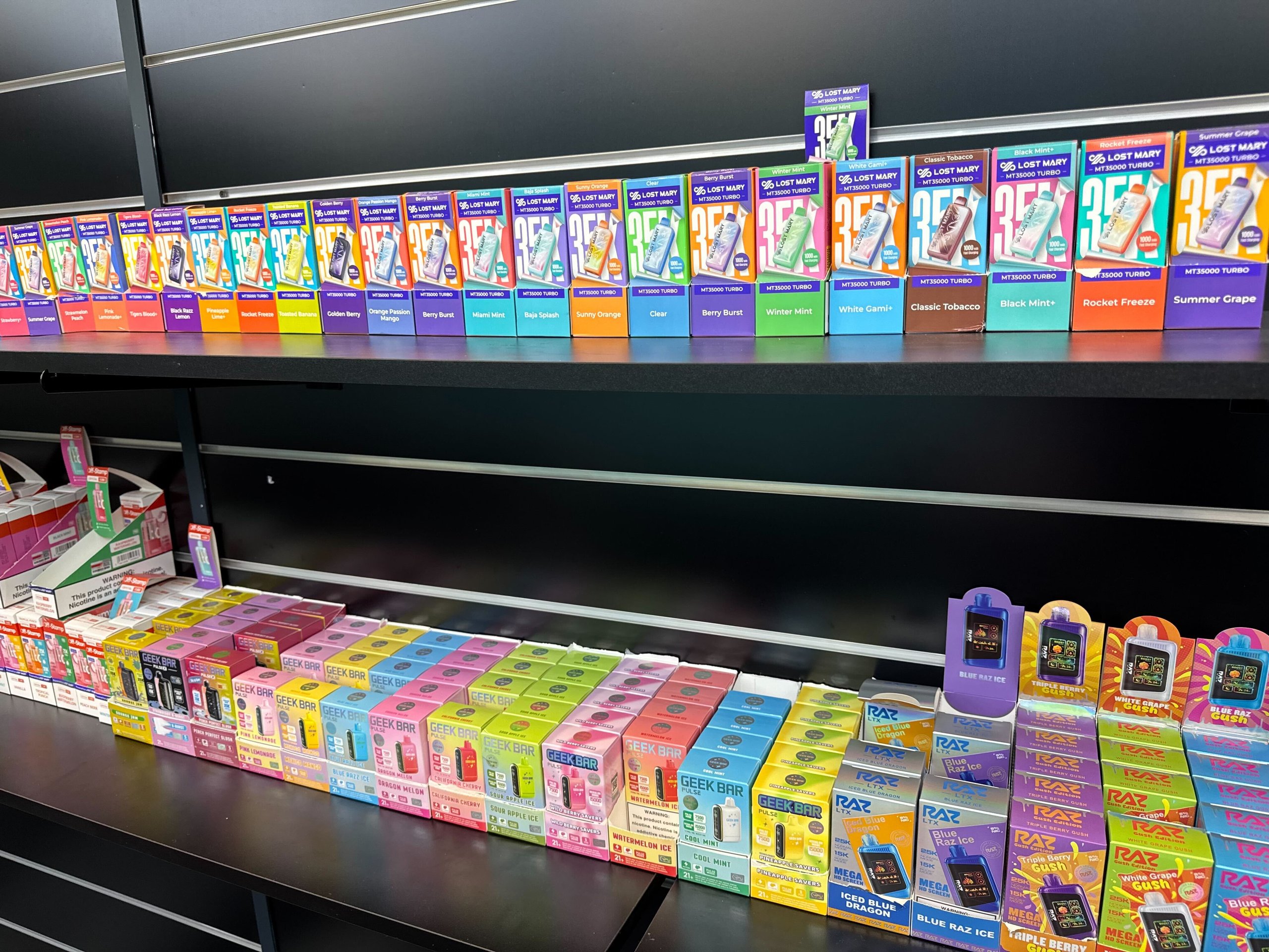 Retail display shelves stocked with colorful Lost Mary and Geek Bar vaping products in various flavors.